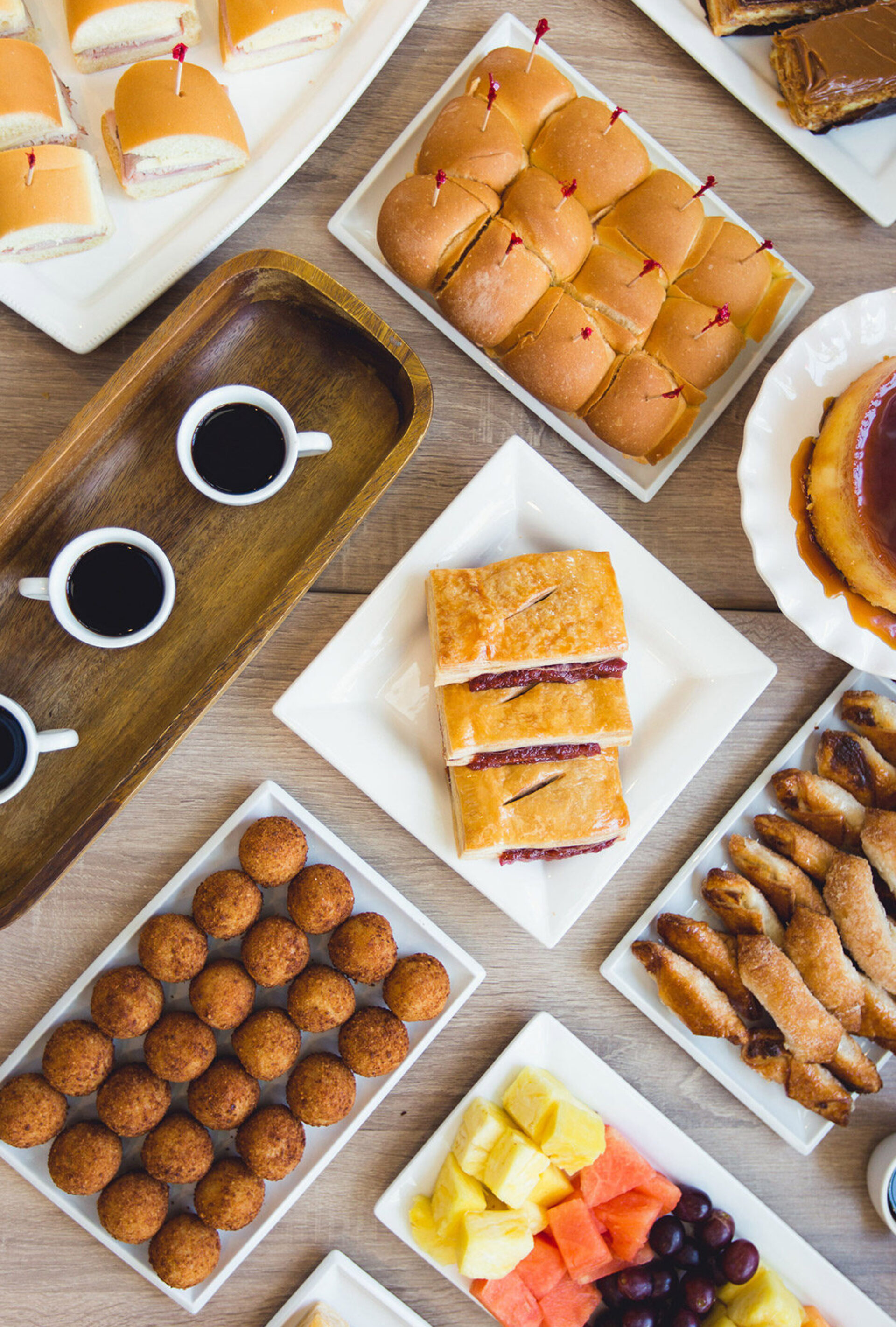 Cuban catering spread, sliders, croquetas, pastelitos, cafecito on a wood table.